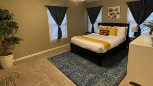 Un dormitorio con cama, ventilador de techo, planta en maceta, escritorio y ventana con cortinas.