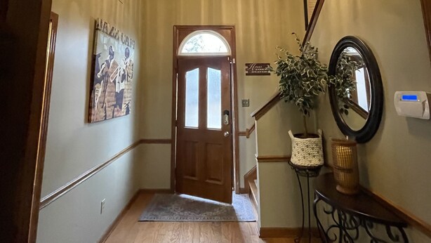 Un pasillo con puerta de madera, candelabro, cuadro enmarcado, espejo y planta en maceta.