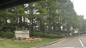 Carretera que lleva a la sede mundial de FedEx Express, con un cartel, una zona verde y una cerca.