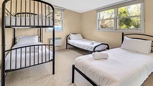 A room with bunk beds, a single bed, and a window with a view of trees.