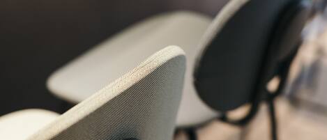 A close-up of a chair with a textured fabric seat and a black armrest.