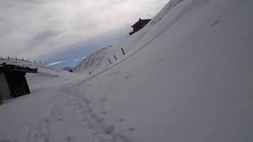 Pendiente nevada con un edificio en la base y un área boscosa al fondo.