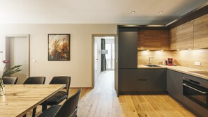 A modern kitchen with wooden cabinets, a dining area with a wooden table and chairs, and a hallway leading to another room. - REMIND Apartments (Brixen im Thale)