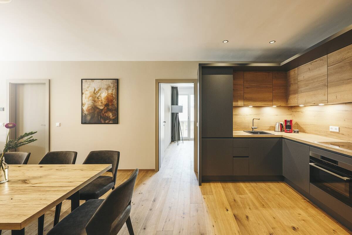 A modern kitchen with wooden cabinets, a dining area with a wooden table and chairs, and a hallway leading to another room.