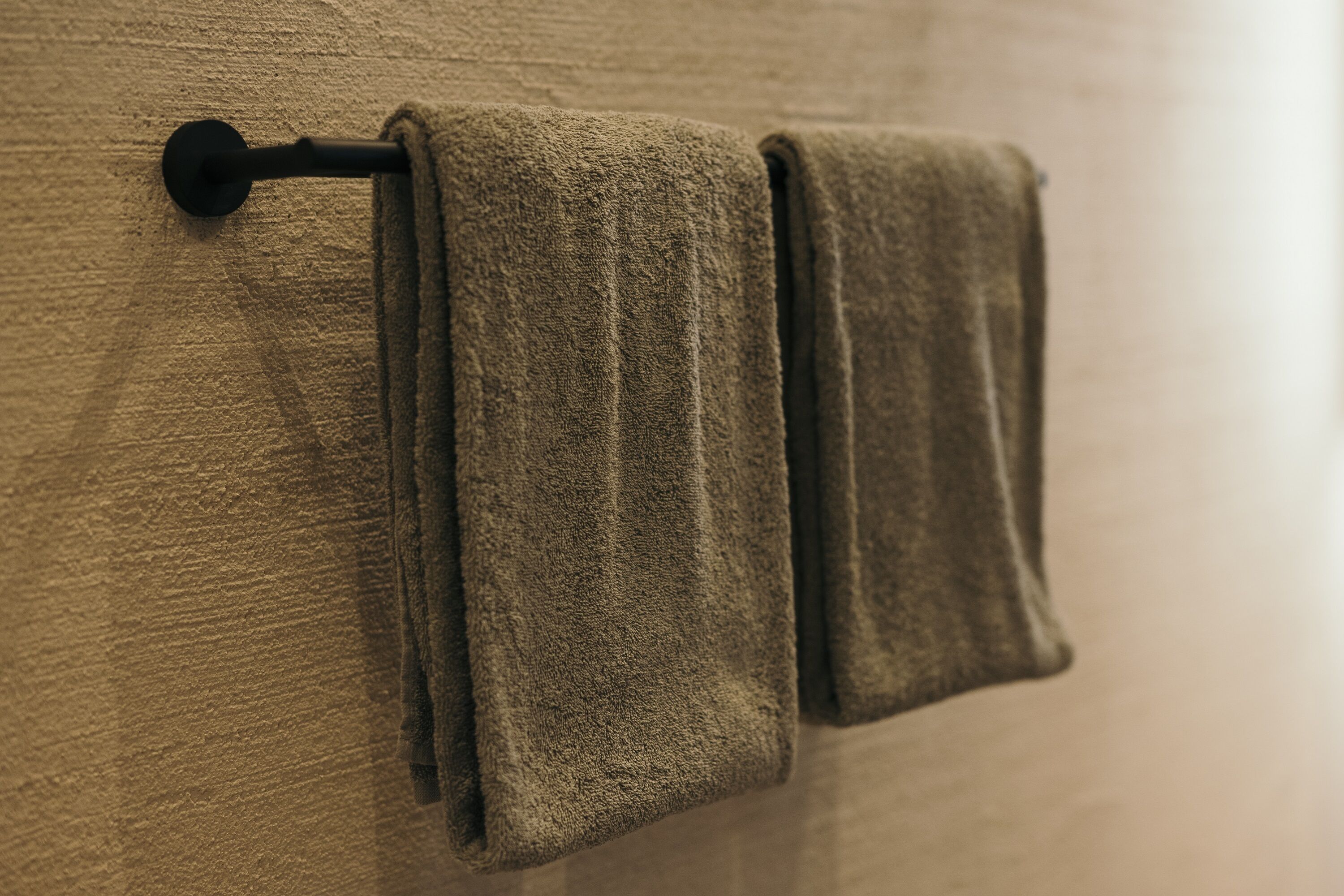 A towel rack with two folded towels against a textured wall.