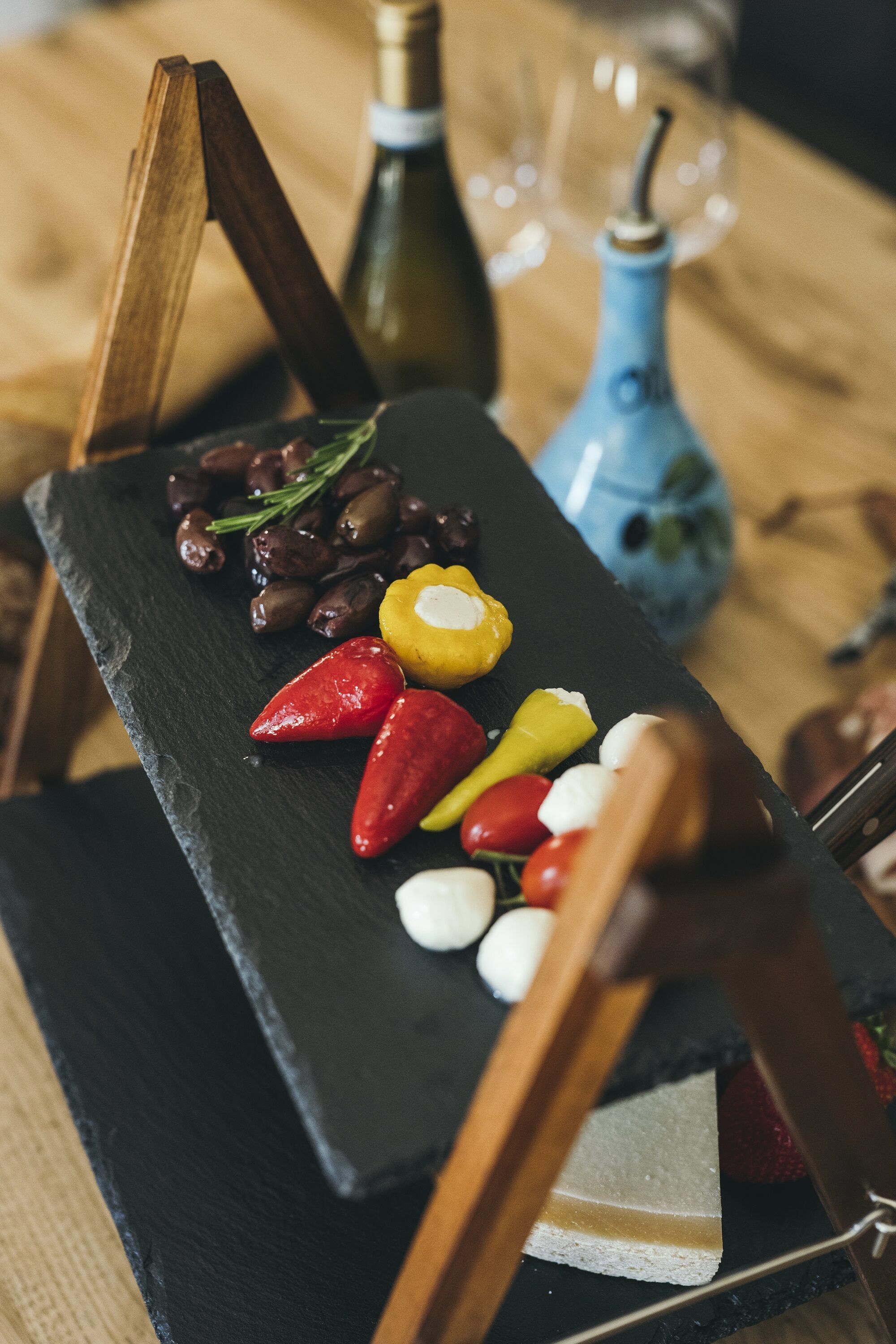A black slate board with various colorful vegetables and a bottle of olive oil.