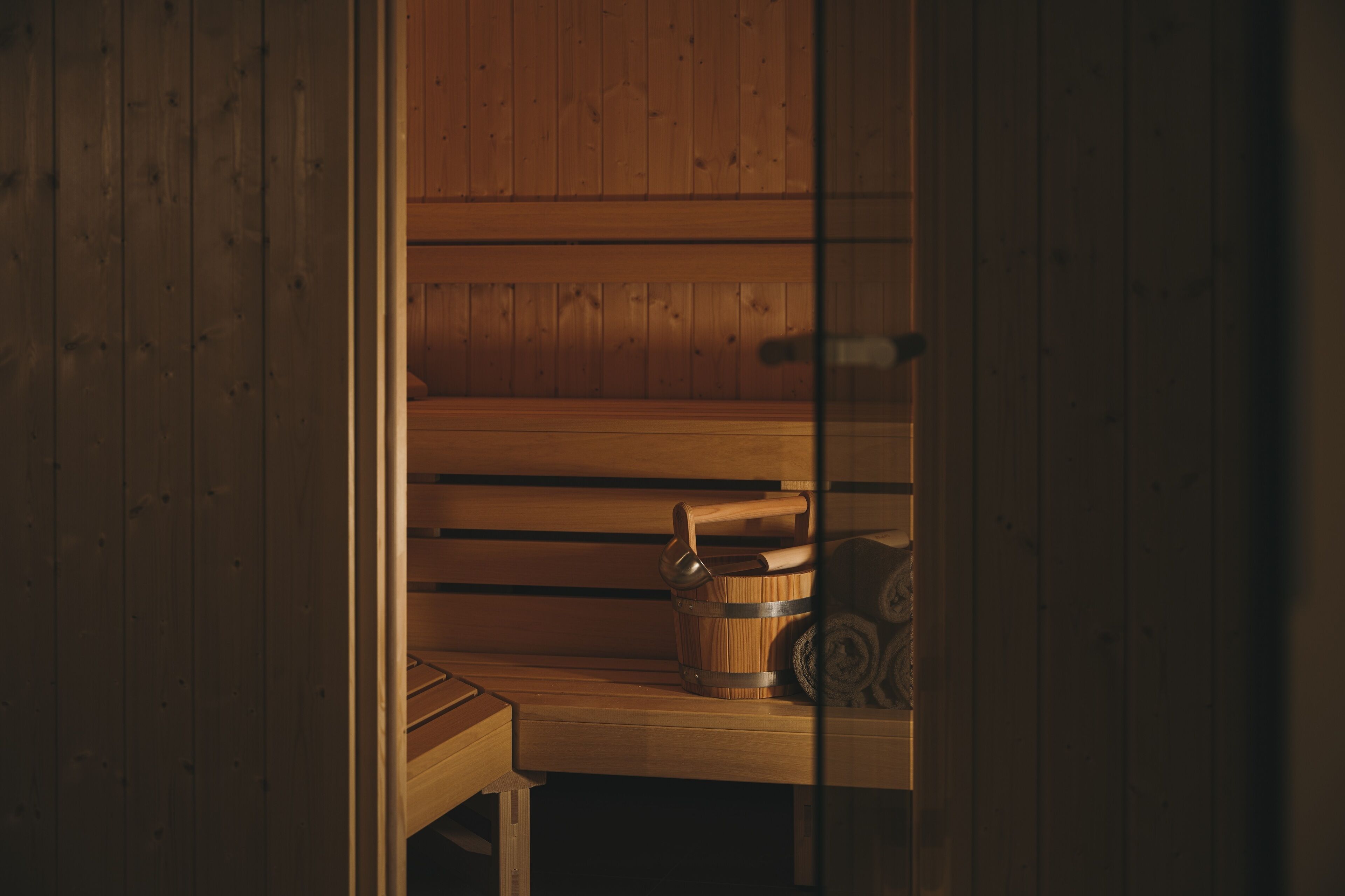 A wooden sauna with benches and a wooden bucket.