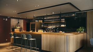 A modern bar area with a wooden counter, bar stools, and a variety of bottles and glasses. - REMIND Apartments (Brixen im Thale)