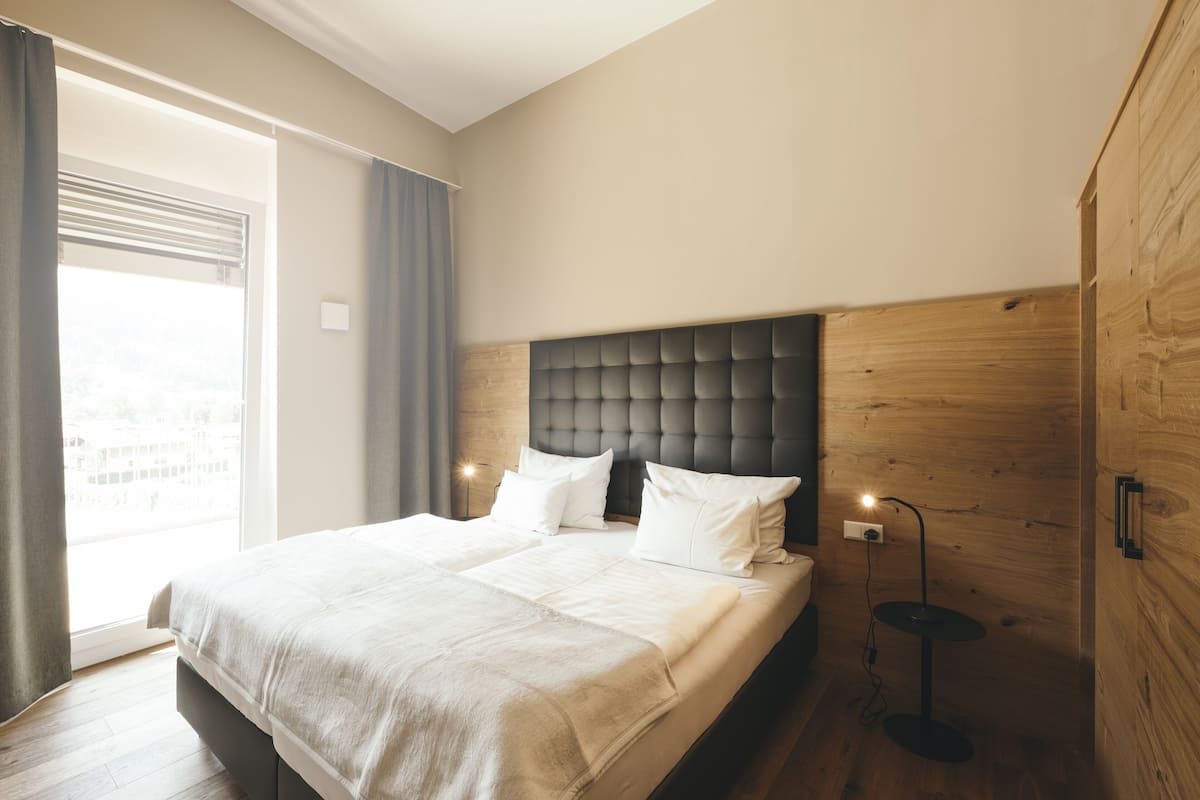 A modern bedroom with a large bed, a wooden headboard, and a bedside table with a lamp.