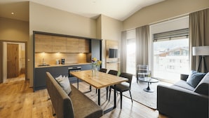 A modern living room with a wooden dining table, grey sofa, and a large window with curtains. - REMIND Apartments (Brixen im Thale)