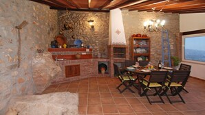 A rustic dining area with a stone wall, a brick fireplace, and a view through a window.