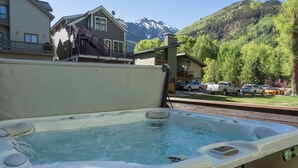 A hot tub with a mountain view, a wooden deck, and a building with a balcony. - Quiet Lofted Studio at Tomboy Lodge (Telluride)