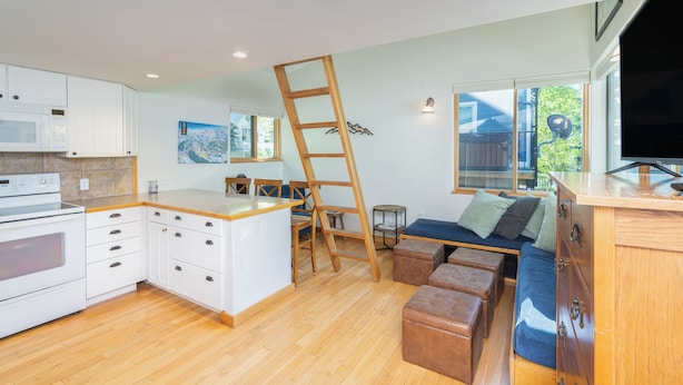 A modern kitchen with white cabinets, a wooden countertop, and a built-in oven. There is a wooden ladder leaning against the wall, a small table with chairs, and a blue sofa with cushions. - Quiet Lofted Studio at Tomboy Lodge (Telluride)