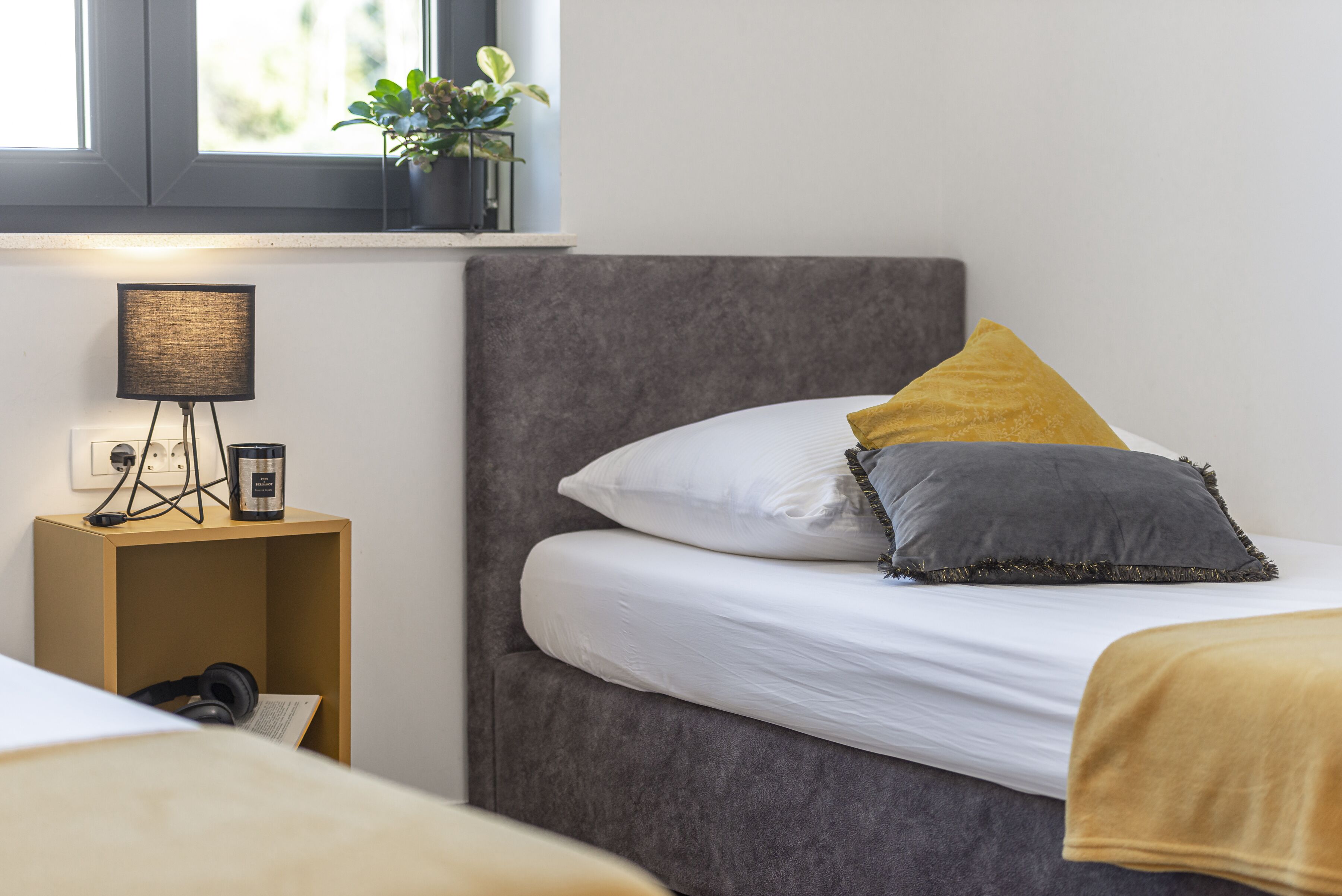 A bedroom with a bed, a bedside table with a lamp, and a window with a plant.