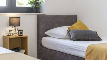 A bedroom with a bed, a bedside table with a lamp, and a window with a plant.