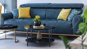 A modern living room with a blue sofa, yellow cushions, a round black coffee table, and a small potted plant. - Apartment Skyline (Konavle)