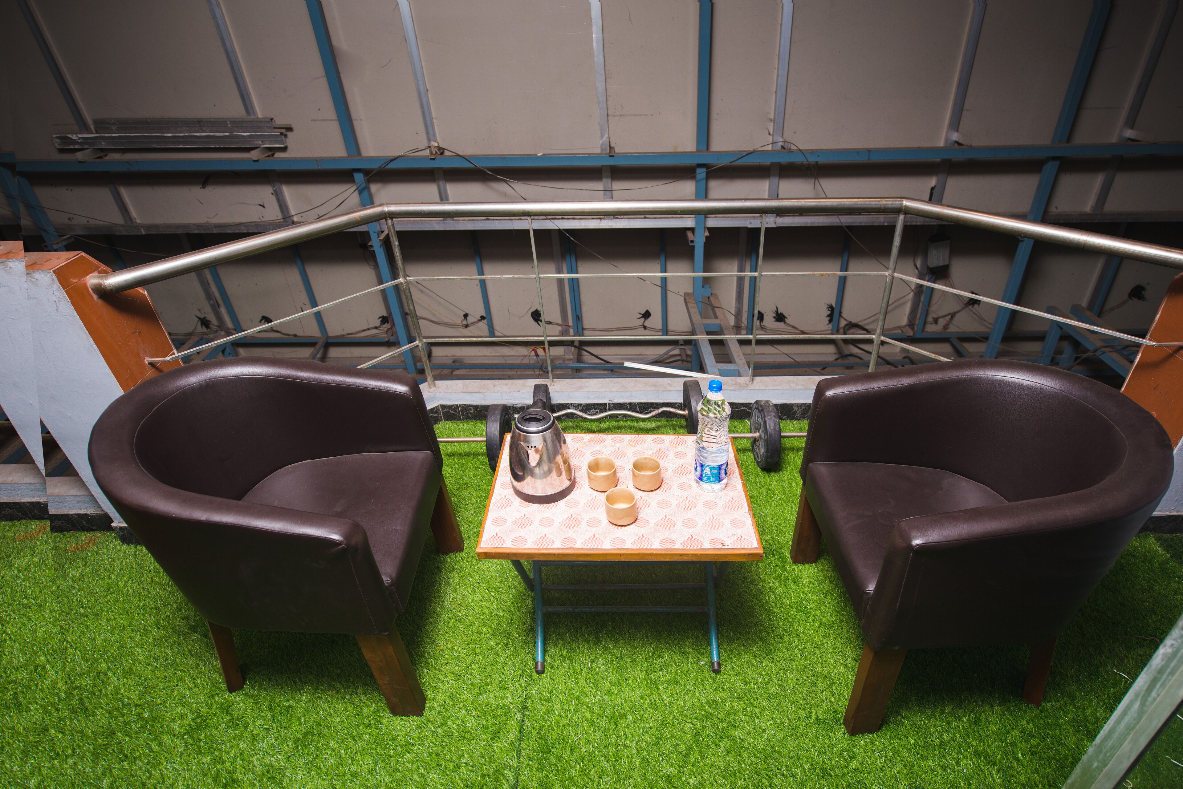 A small room with two brown leather chairs, a table with a kettle, cups, and a water bottle.