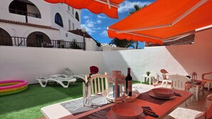 An outdoor dining area with a table set for two, surrounded by white chairs and orange umbrellas. - Casa Teide, ground floor Parque Santiago 1, heated pool, 100 m to sea+beach (Playa de la Américas)