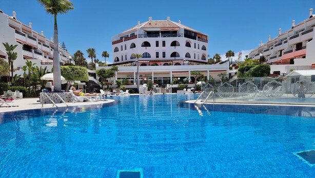 A large swimming pool with lounge chairs and a building with multiple balconies in the background. - Casa Teide, ground floor Parque Santiago 1, heated pool, 100 m to sea+beach (Playa de la Américas)
