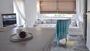 A modern room with a large window, a sofa, a dining table, and a TV. - Koukounari Cottage Paros, Apartment With sea View (Paros)
