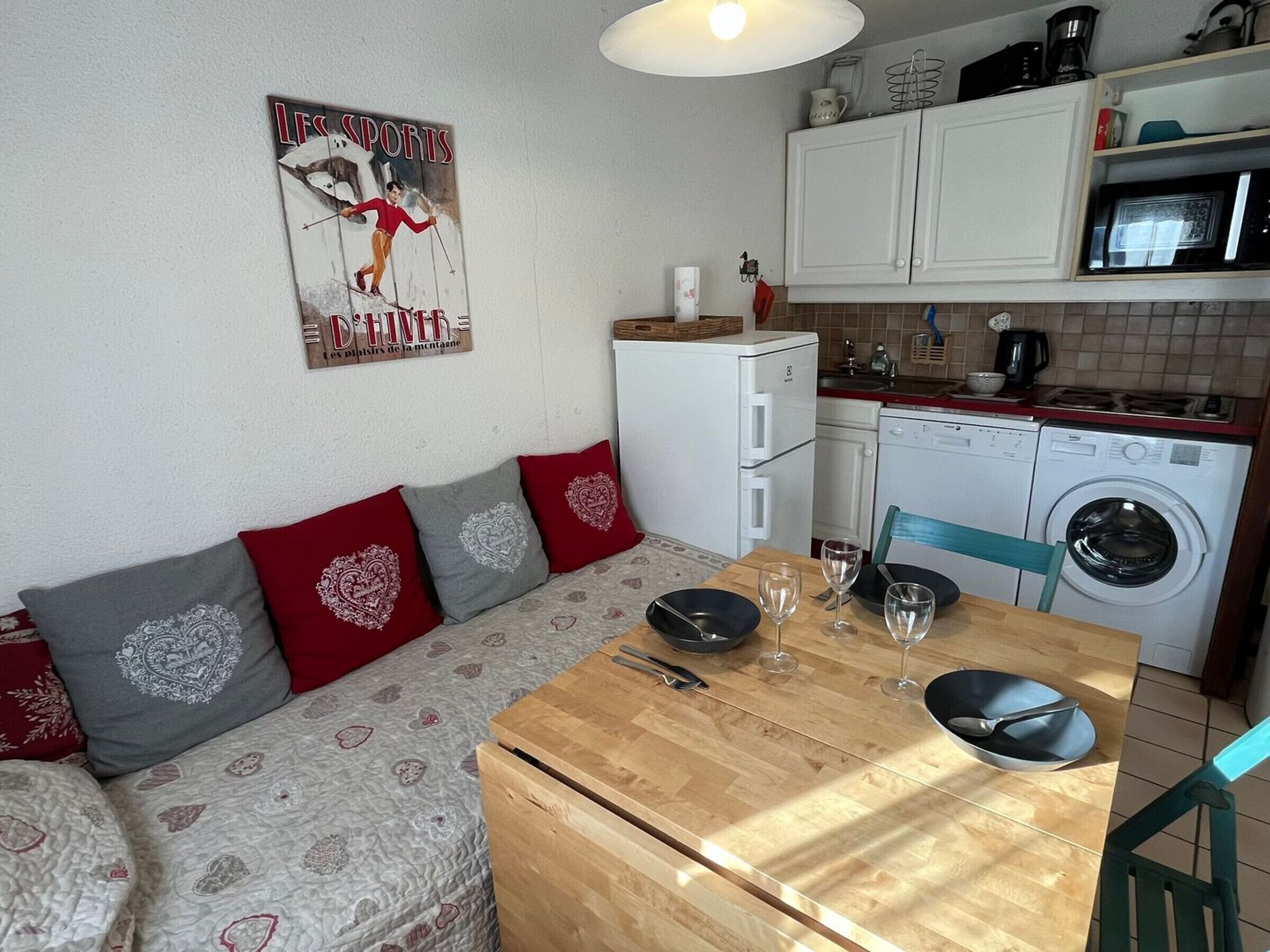 Un espacio habitable compacto con sofá, mesa de comedor, lavadora y zona de cocina.