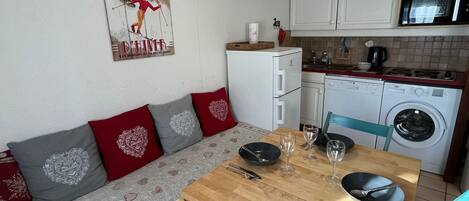 Un espacio habitable compacto con sofá, mesa de comedor, lavadora y zona de cocina.