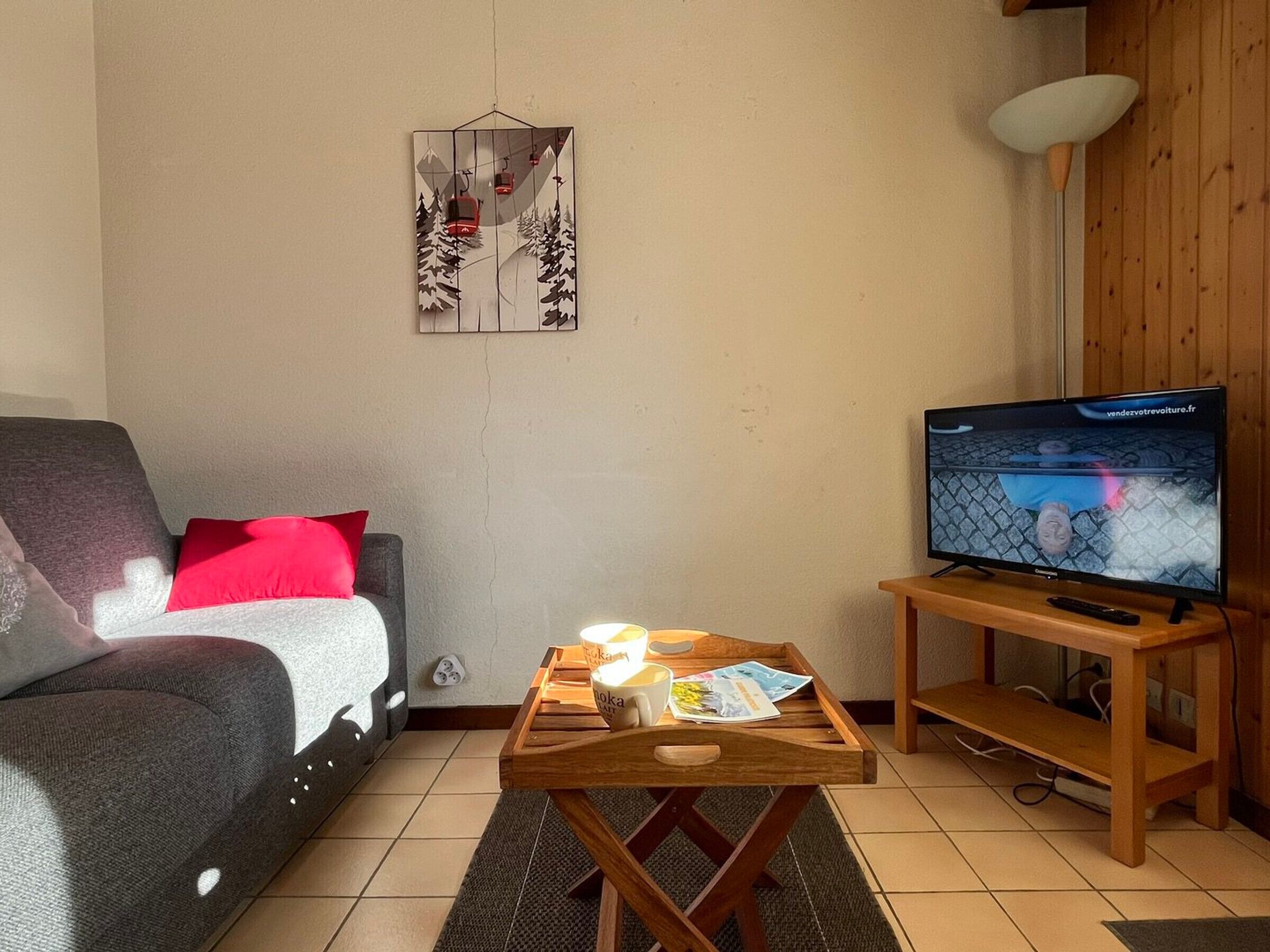 Olohuone, jossa on sohva, sohvapöytä, jossa on lehti, jalustalla oleva televisio ja seinäkoriste.