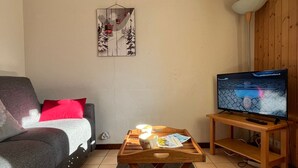 A living room with a sofa, a coffee table with a magazine, a TV on a stand, and a wall decoration.