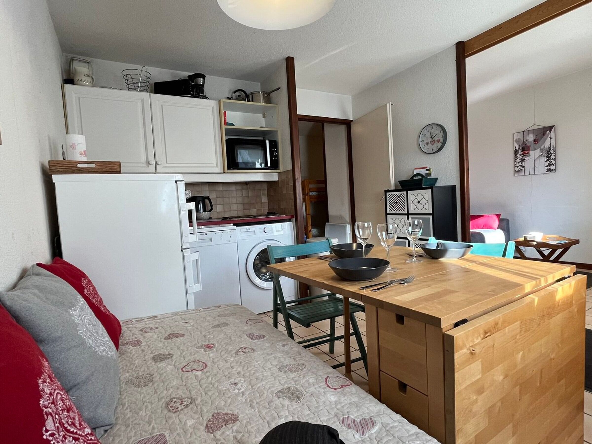 Cocina compacta con microondas, estufa y lavadora. Hay un comedor con mesa y sillas, además de un sofá con funda estampada.