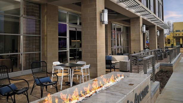 An outdoor seating area with a fire feature, tables, chairs, and a stone wall with the name 'Avenue'. - AC Hotel by Marriott Jackson Ridgeland (Ridgeland)