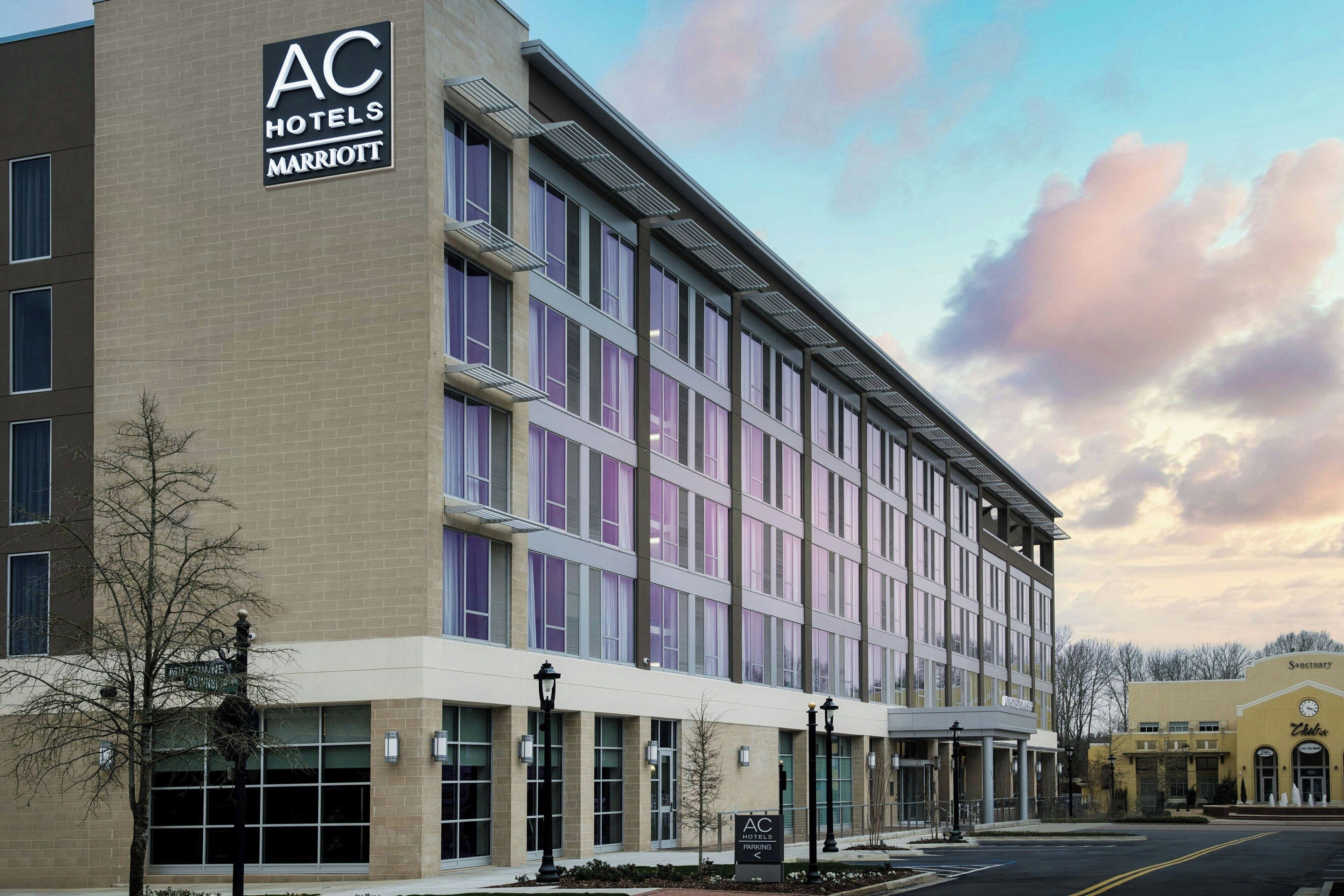A modern hotel with a large sign for AC Hotels Marriott, featuring a brick facade and large windows.