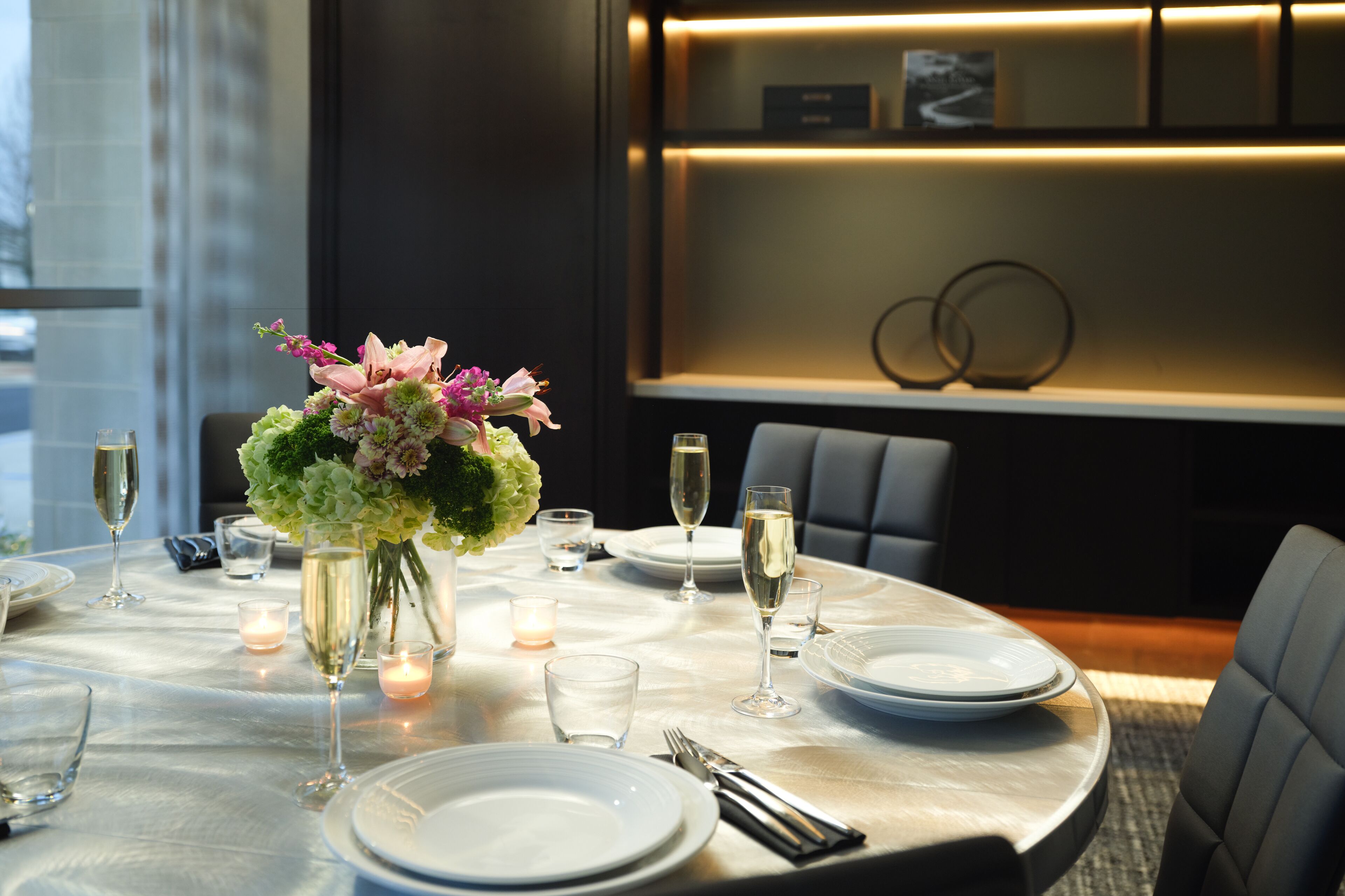A dining table set for a meal with plates, glasses, and a vase of flowers.