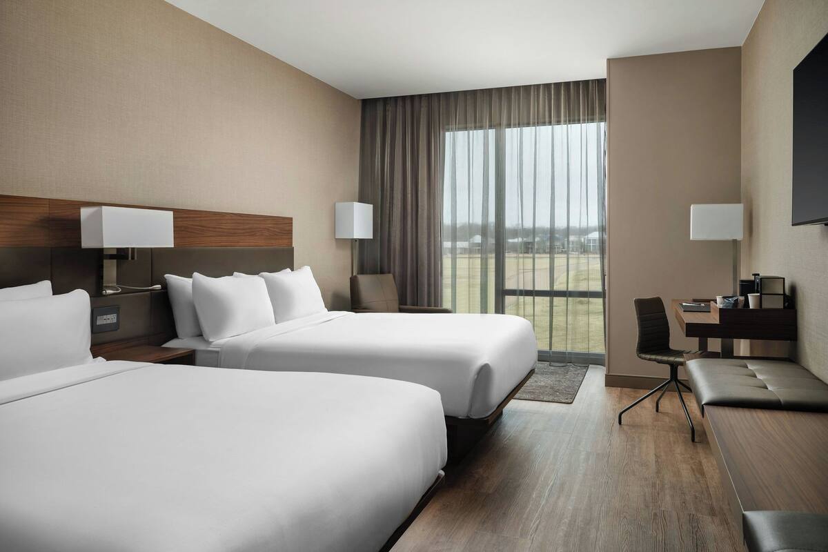 A hotel room with two beds, a desk, a chair, and a TV.