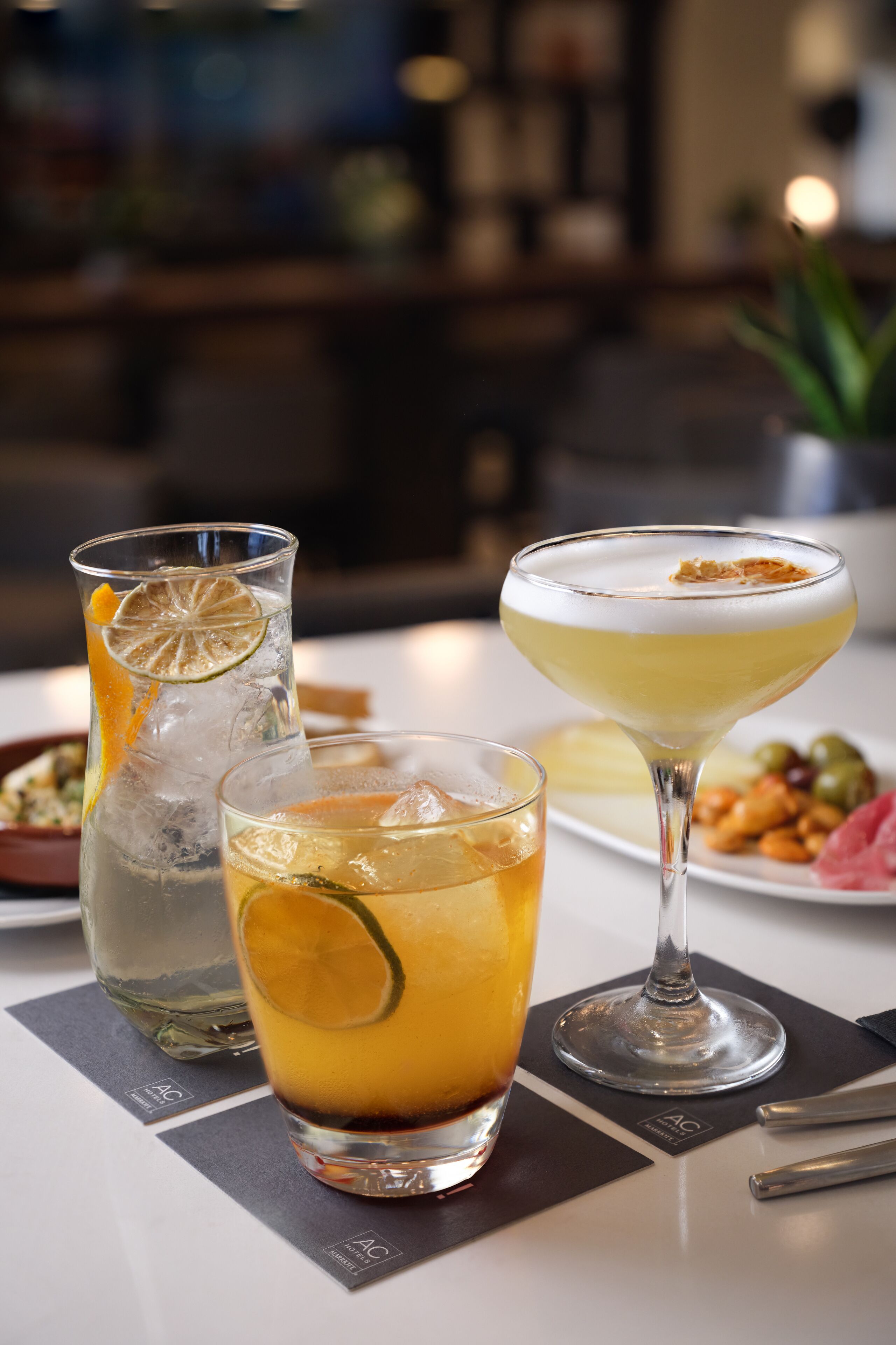 A table with three drinks, a pitcher, and a plate of nuts.