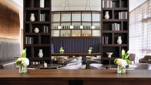 A modern hotel lobby with a central dining table, seating arrangements, and a large bookshelf filled with books and decorative items. - AC Hotel by Marriott Jackson Ridgeland (Ridgeland)