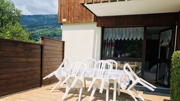 Un terrazzo in legno con tavolo e sedie, una recinzione in legno e vista su una catena montuosa.