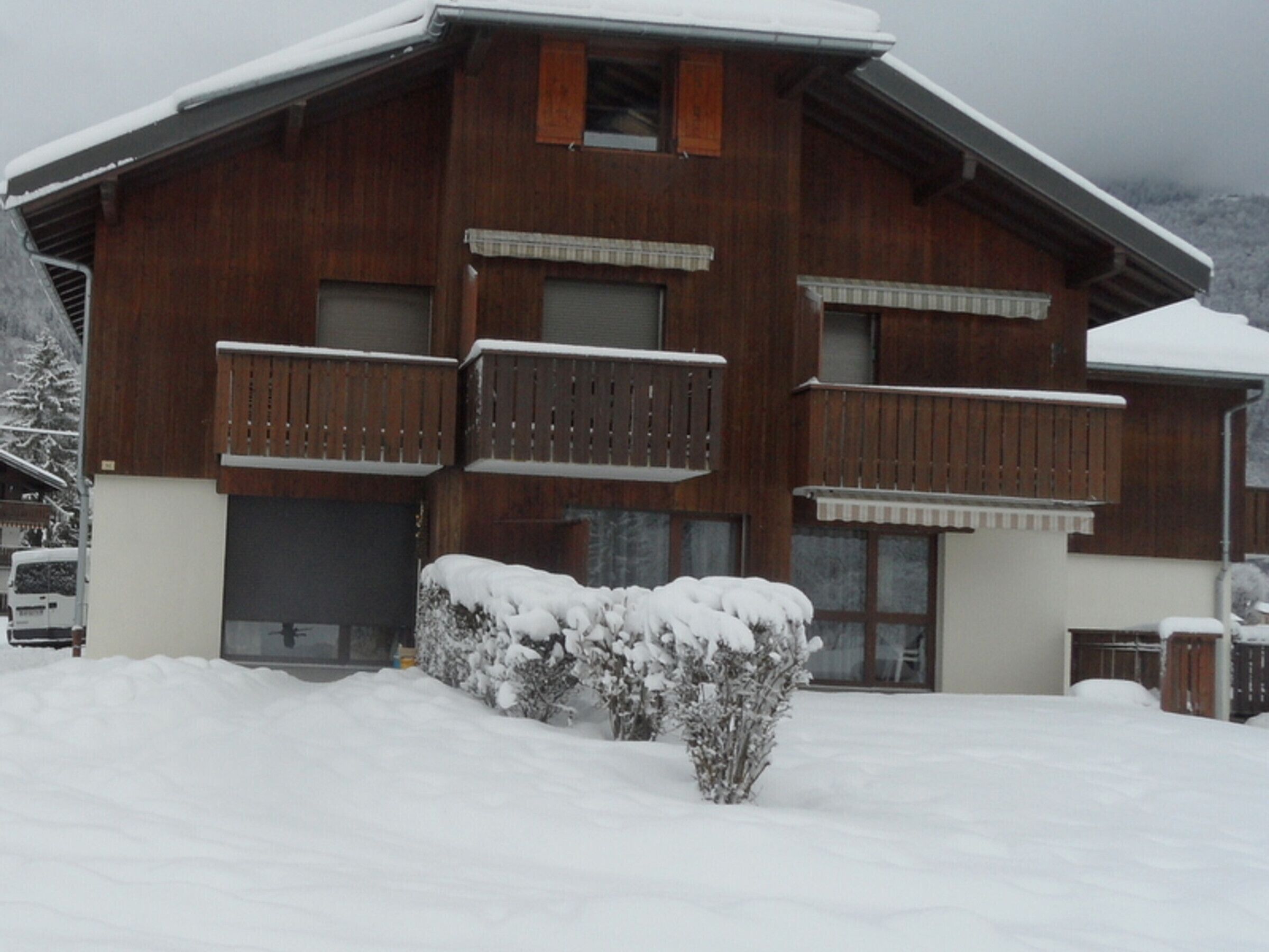 A wooden chalet with multiple balconies, a garage, and a snow-covered landscape.
