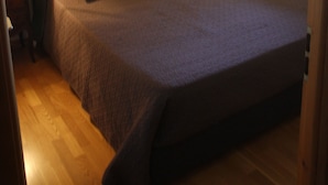 Un dormitorio con una cama grande, una mesita de noche con lámpara, un cuadro en la pared y una ventana con cortinas.