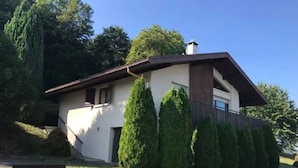Una casa moderna de dos plantas con techo inclinado, rodeada de setos y árboles bien cuidados.