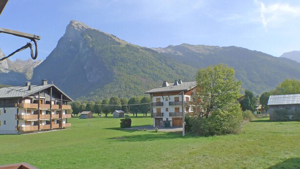 A mountain lodge with multiple balconies, a grassy field, and a mountain backdrop.