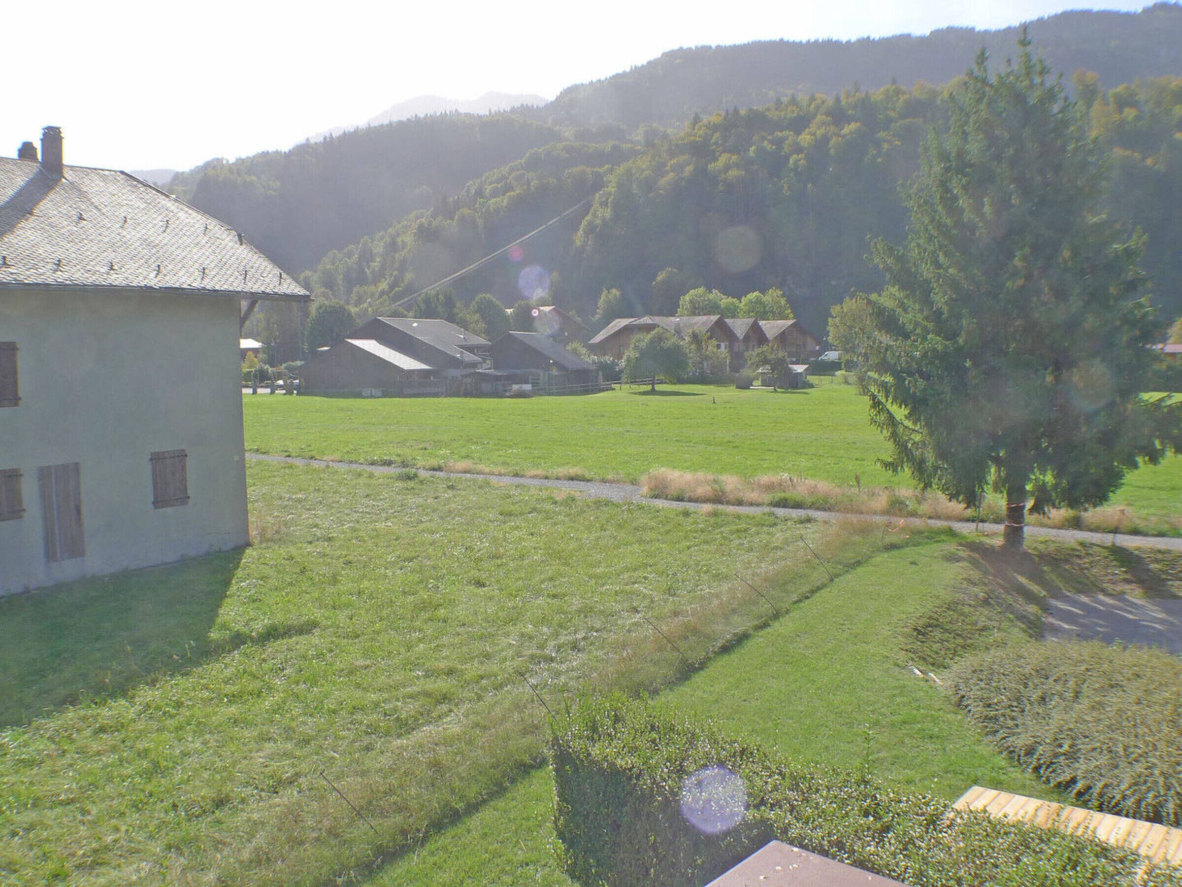A rural setting with a white building, green fields, and a forested hill in the background.