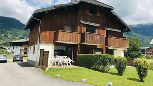 A two-story wooden building with balconies, a paved driveway, and a grassy area with chairs.
