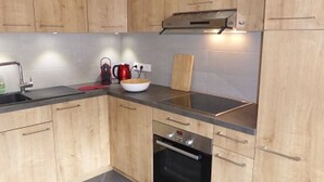 Eine Küche mit Holzausstattung, einer schwarzen Arbeitsplatte, einem Spülbecken, einem Wasserkocher, einem Schneidebrett und einem Backofen.