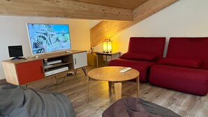 Ein gemütliches Wohnzimmer mit Fernseher, rotem Sofa und Sitzsäcken.
