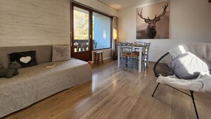 Un soggiorno moderno con un divano, una poltrona, un tavolo da pranzo con sedie, un'ampia finestra e una lampada a soffitto.