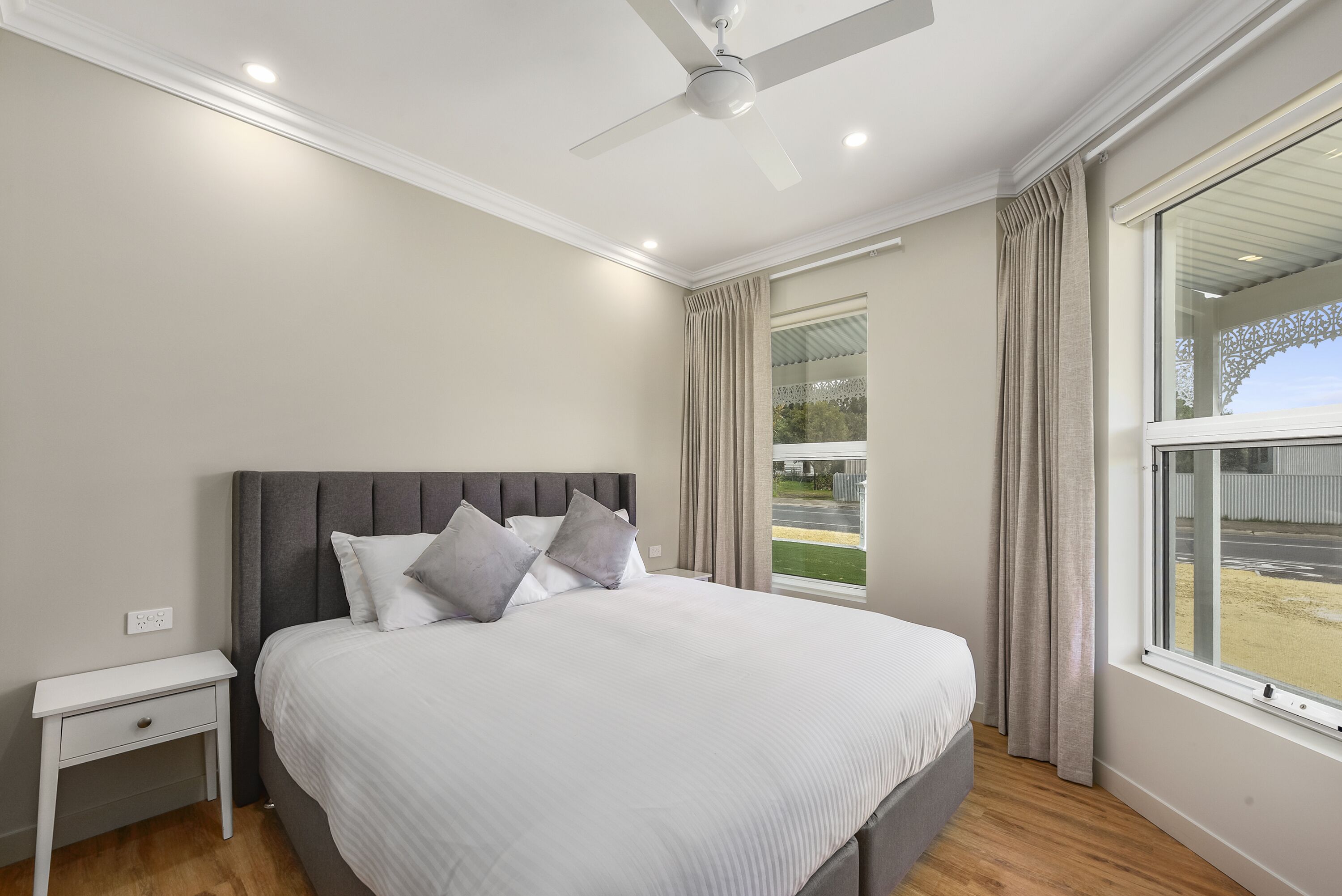 A modern bedroom with a large bed, a nightstand, a ceiling fan, and a window with curtains.