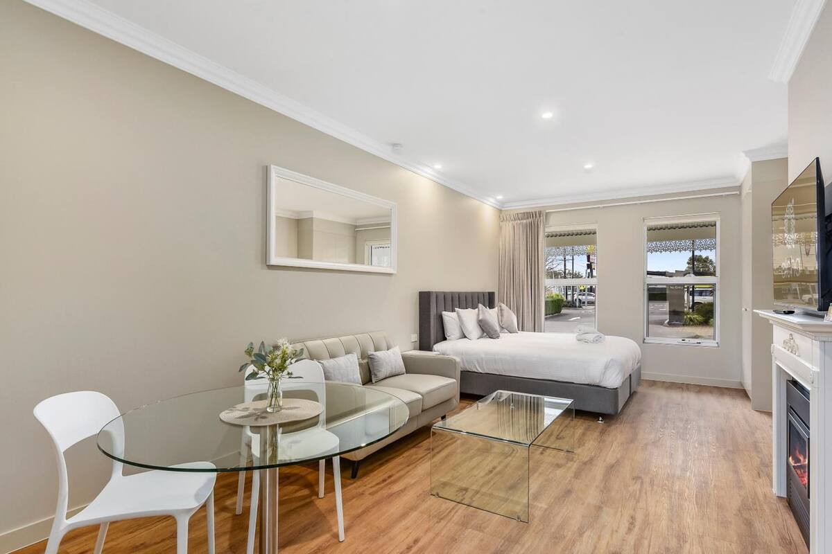 Una habitación de hotel moderna con cama, sofá, mesa de vidrio y televisión.