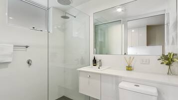 Une salle de bain moderne avec une douche à parois de verre, un lavabo blanc avec un miroir au-dessus et des toilettes.