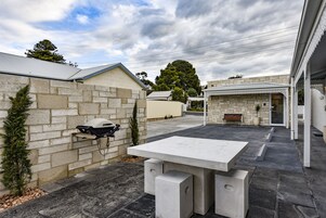 Un patio con una mesa de hormigón y una barbacoa, rodeado de muros de piedra y un edificio de ladrillo.