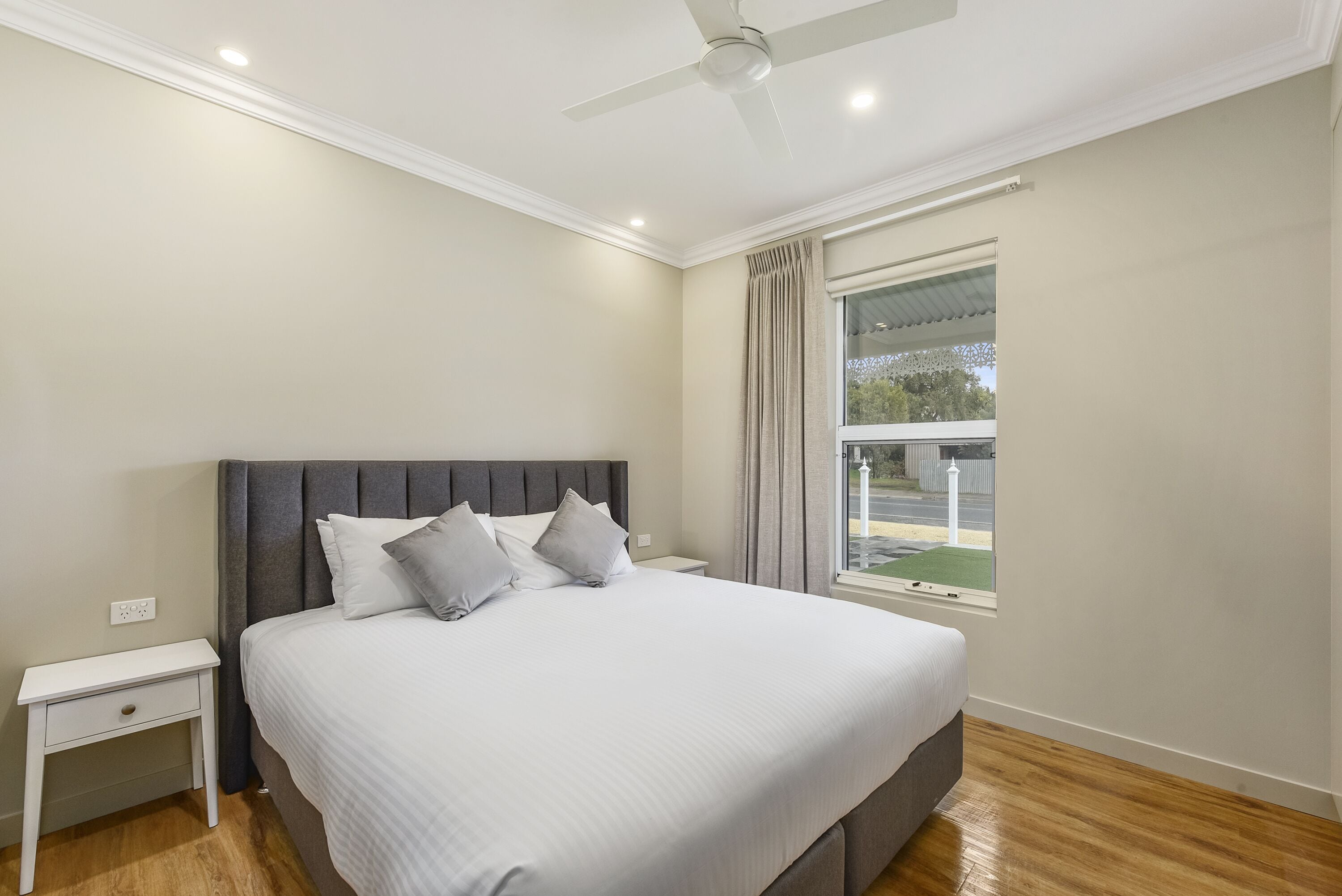 A bedroom with a large bed, a nightstand, a ceiling fan, and a window with curtains.